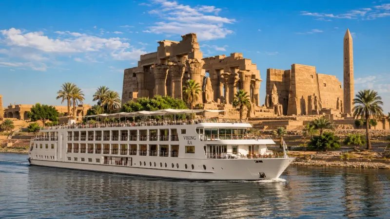 A premium river cruise ship sailing along the Nile River in Luxor past ancient Egyptian temples, an organized tour by Piccola Travel, a travel agency in Miami.