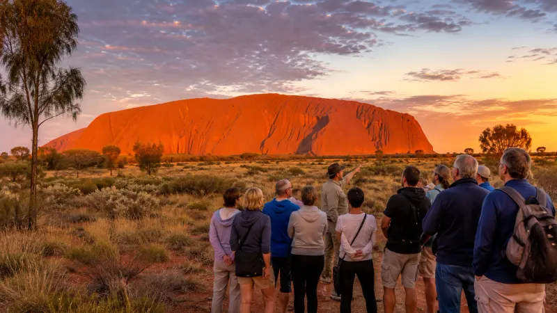 A guided group of travelers watching the sunset glow over the massive red sandstone monolith of Uluru in the Australian Outback.