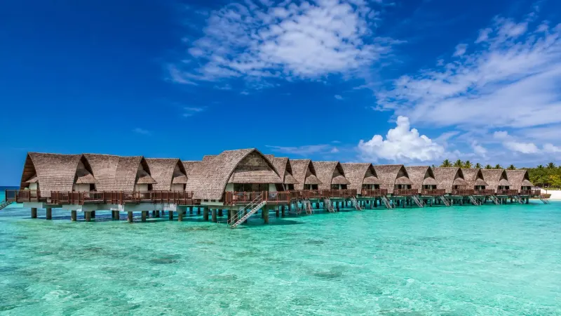 Traditional overwater bungalows stretching over a crystal clear blue lagoon at a luxury all-inclusive resort in Fiji, planned by Piccola Travel in Miami, Florida.