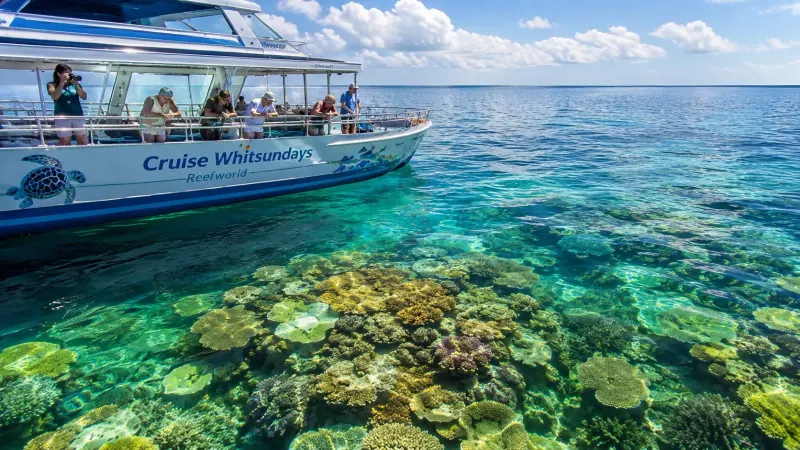 Aerial view of a luxury catamaran sailing over the vibrant coral formations of the Great Barrier Reef in Australia.