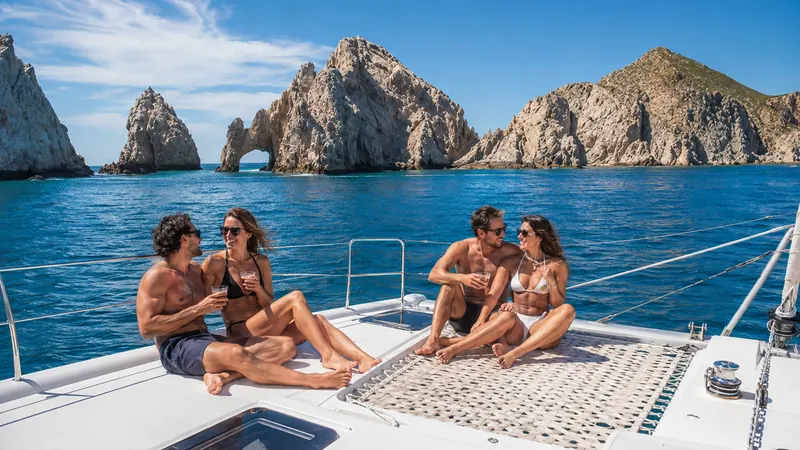 Friends sailing a catamaran past the Arch of Cabo San Lucas