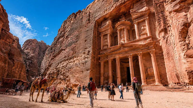 Petra's rose-red Treasury carved into sandstone cliffs, camels resting at its base — Petra Treasury tour.