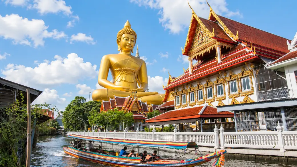 Giant seated golden Buddha rising over a canal-side temple in Bangkok on a guided Thailand tour
