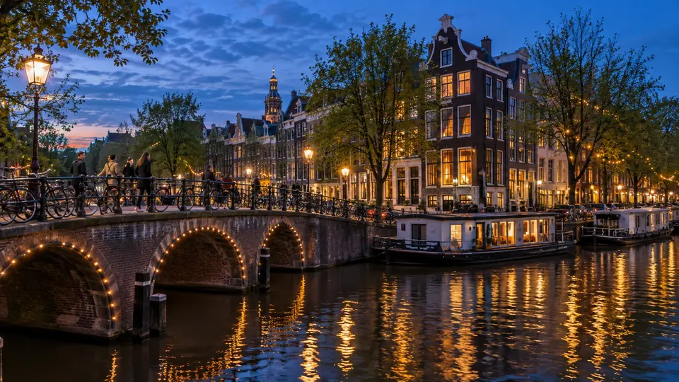 An Amsterdam canal at blue hour with lit canal houses, houseboats and bicycles on the bridge