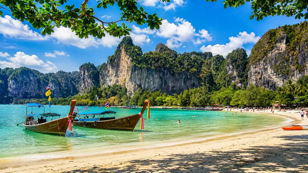 White sand and turquoise sea lined with palms and long-tail boats on a Phuket beach in Thailand