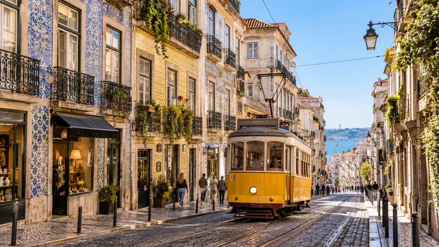 A yellow tram climbing a street in Lisbon's Chiado district in the sun