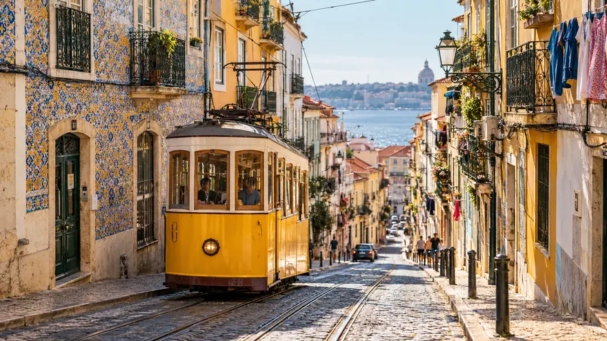 Un tranvía amarillo subiendo una calle estrecha de azulejos en el barrio de Alfama, Lisboa