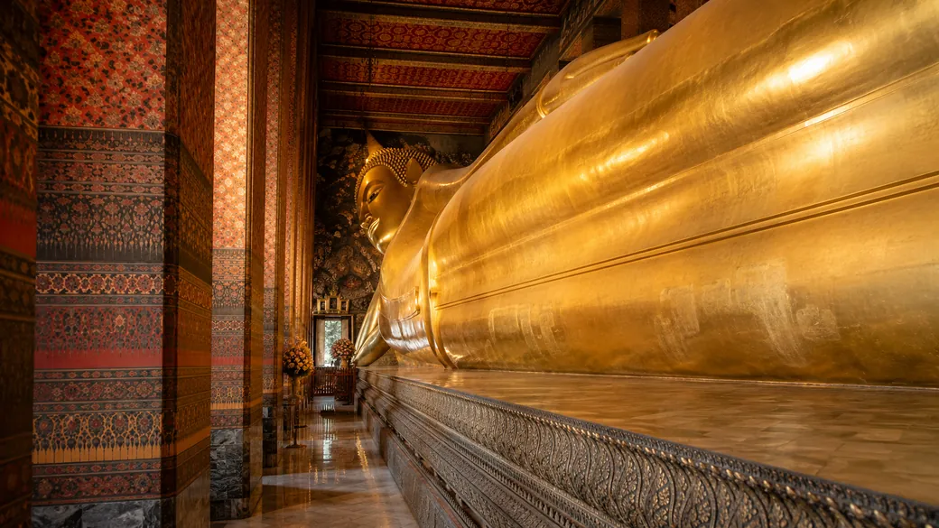The golden Reclining Buddha of Wat Pho stretching along ornate columns in Bangkok, a highlight of this Thailand tour