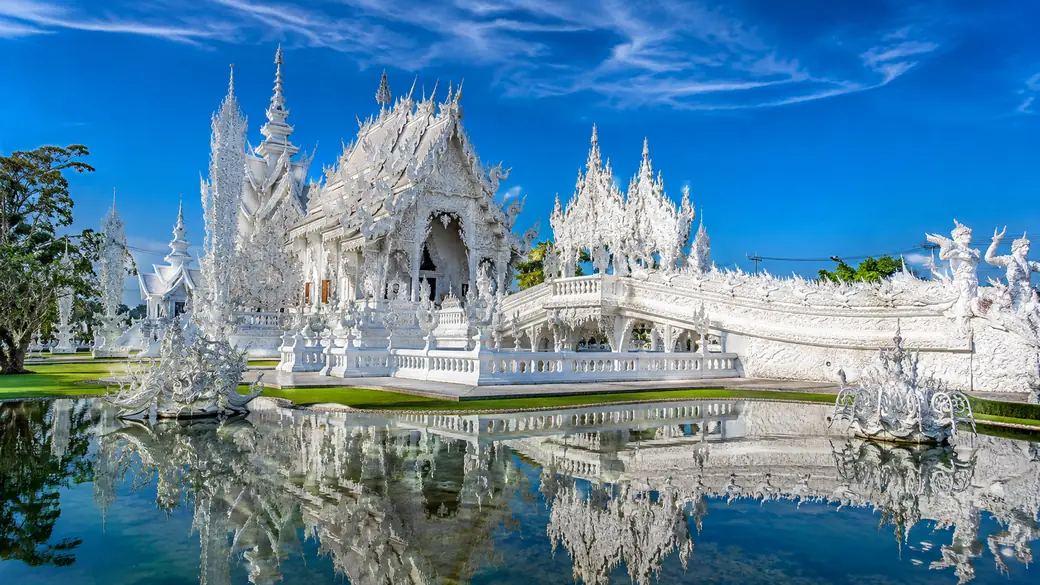 The mirrored white facade of Wat Rong Khun, Chiang Rai's White Temple, reflected in still water on a guided tour
