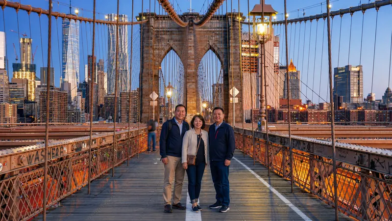 Brooklyn Bridge walkway leading into the Manhattan skyline at dusk — New York City tours and vacations.