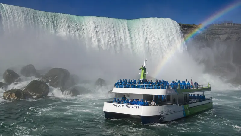 Tour boat in the mist beneath Niagara Falls with a rainbow — Niagara Falls and Toronto tours.